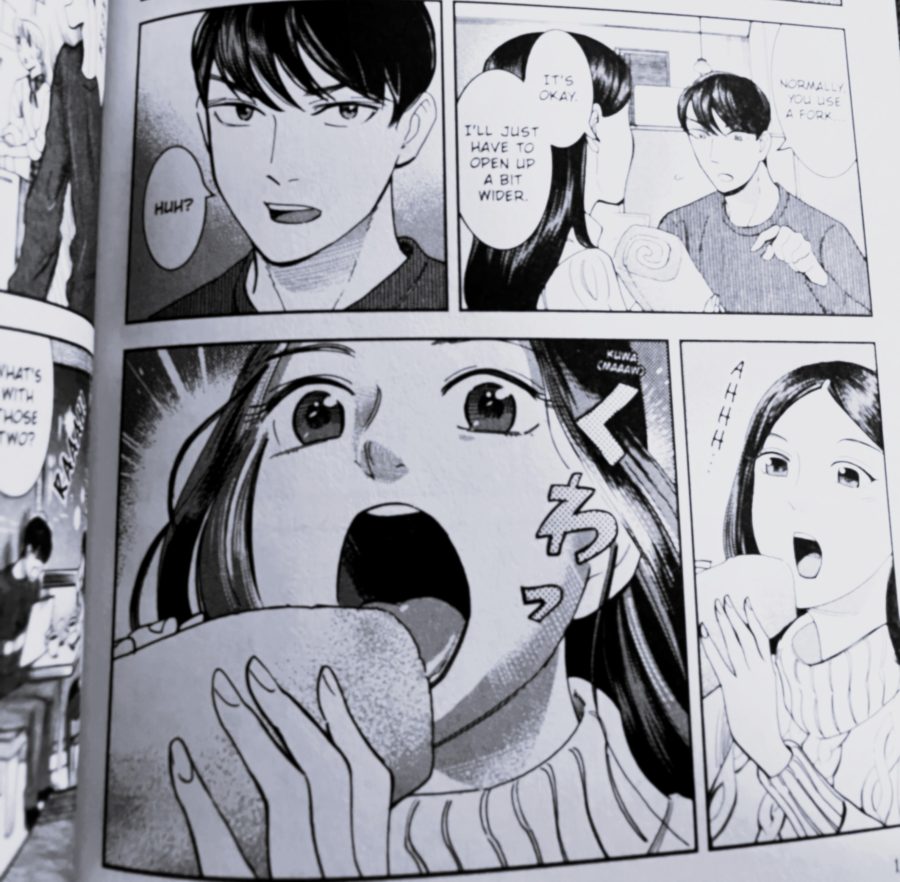 Dark-haired girl opens her mouth wide to fit in a large rolled cake.