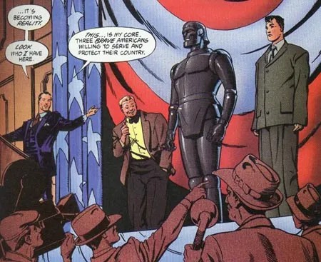 A man in a suit introduces a crowd to three other men, two in suits, one a metal robot, with an American flag draped behind them